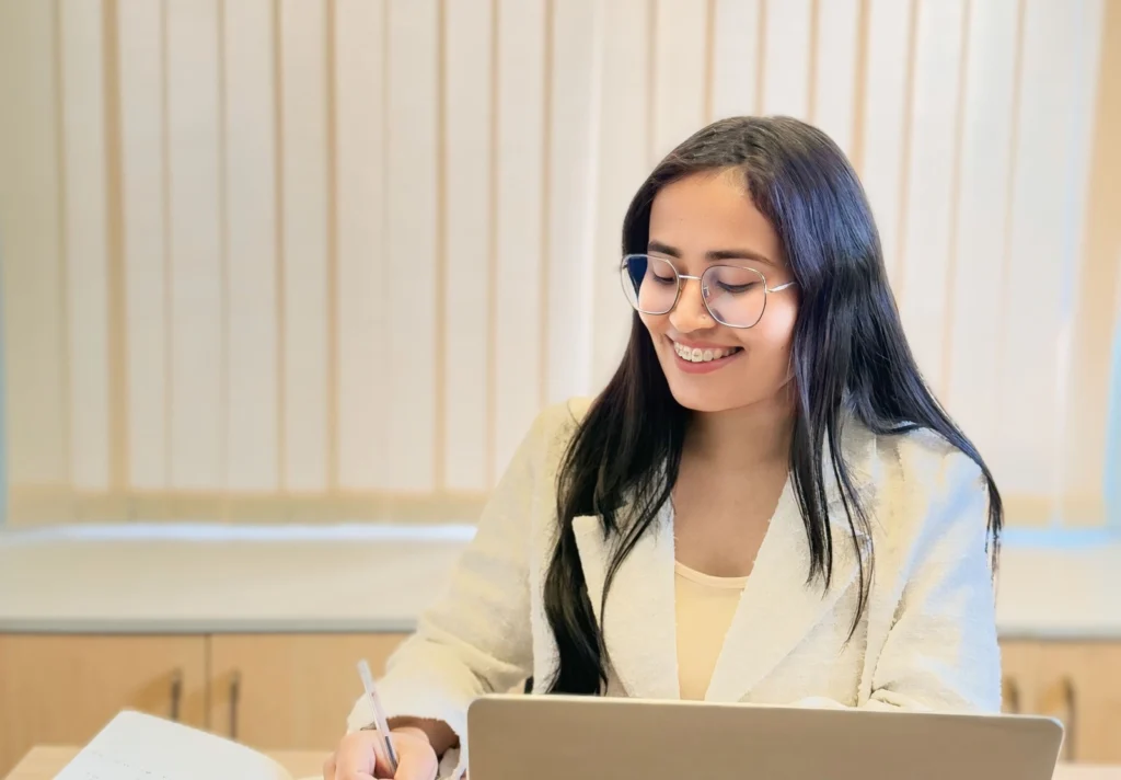 Sudeshna Thapa smiling as she works on a laptop and takes notes
